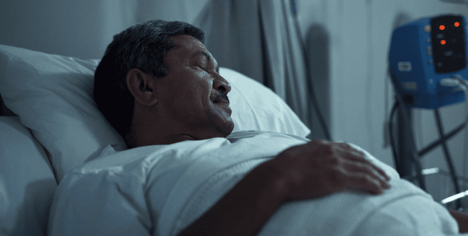 A man lies asleep in a hospital bed. 