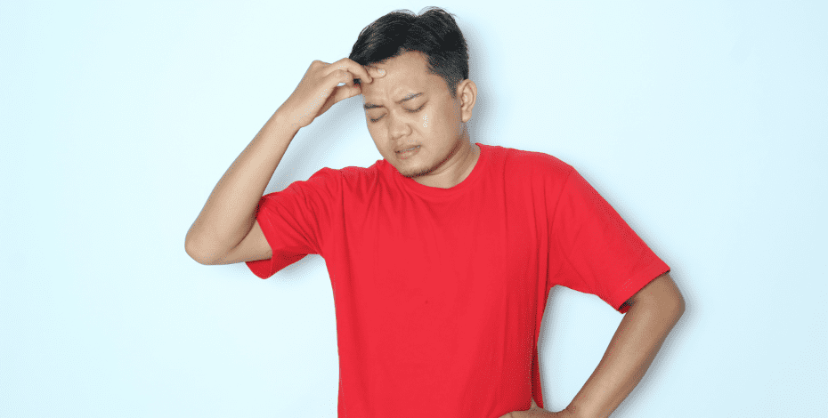 A man in a red shirt has his hand to his forehead