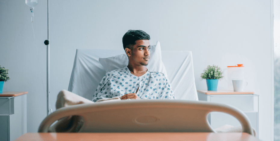 A man with dark hair and olive skin is sitting in a hospital bed