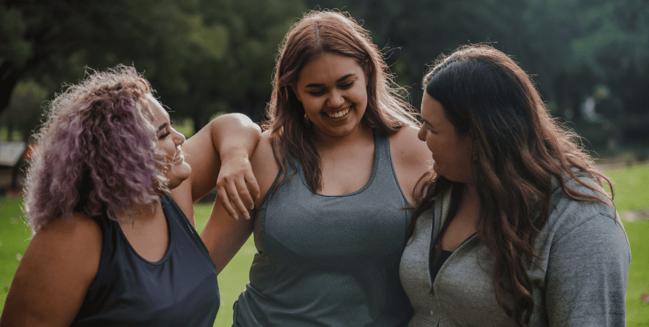 Three indigenous women smiling with their arms around each other. 