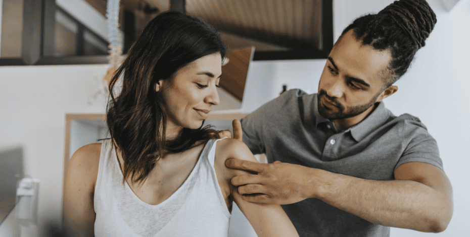 A physiotherapist examines the shoulder of a patient as if in the hospital setting.