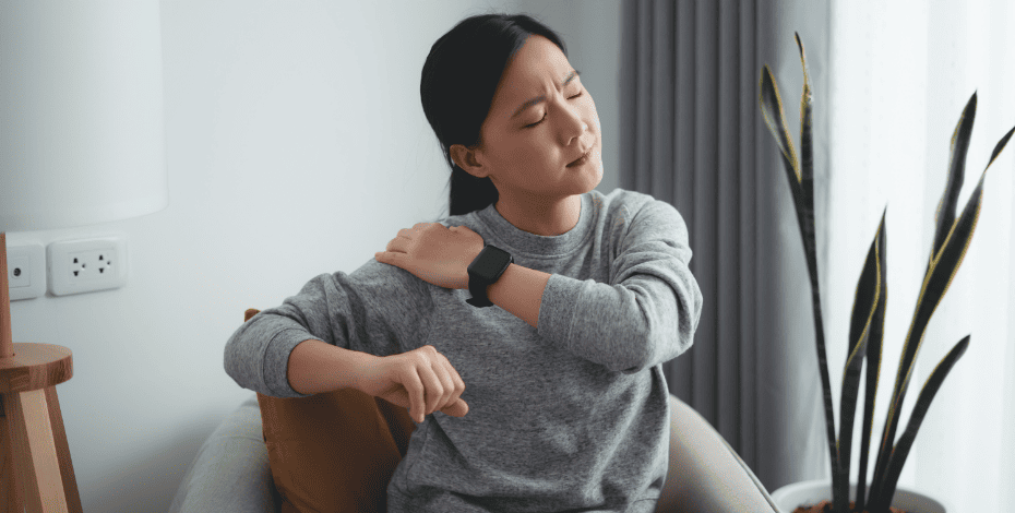 A woman stretches her shoulder, in pain.