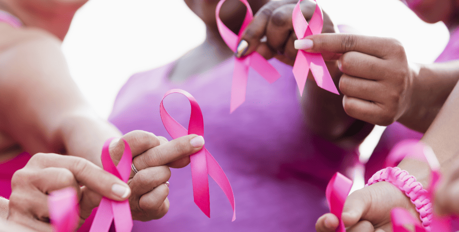 The image focuses on hands holding breast cancer awareness ribbons towards the camera. 