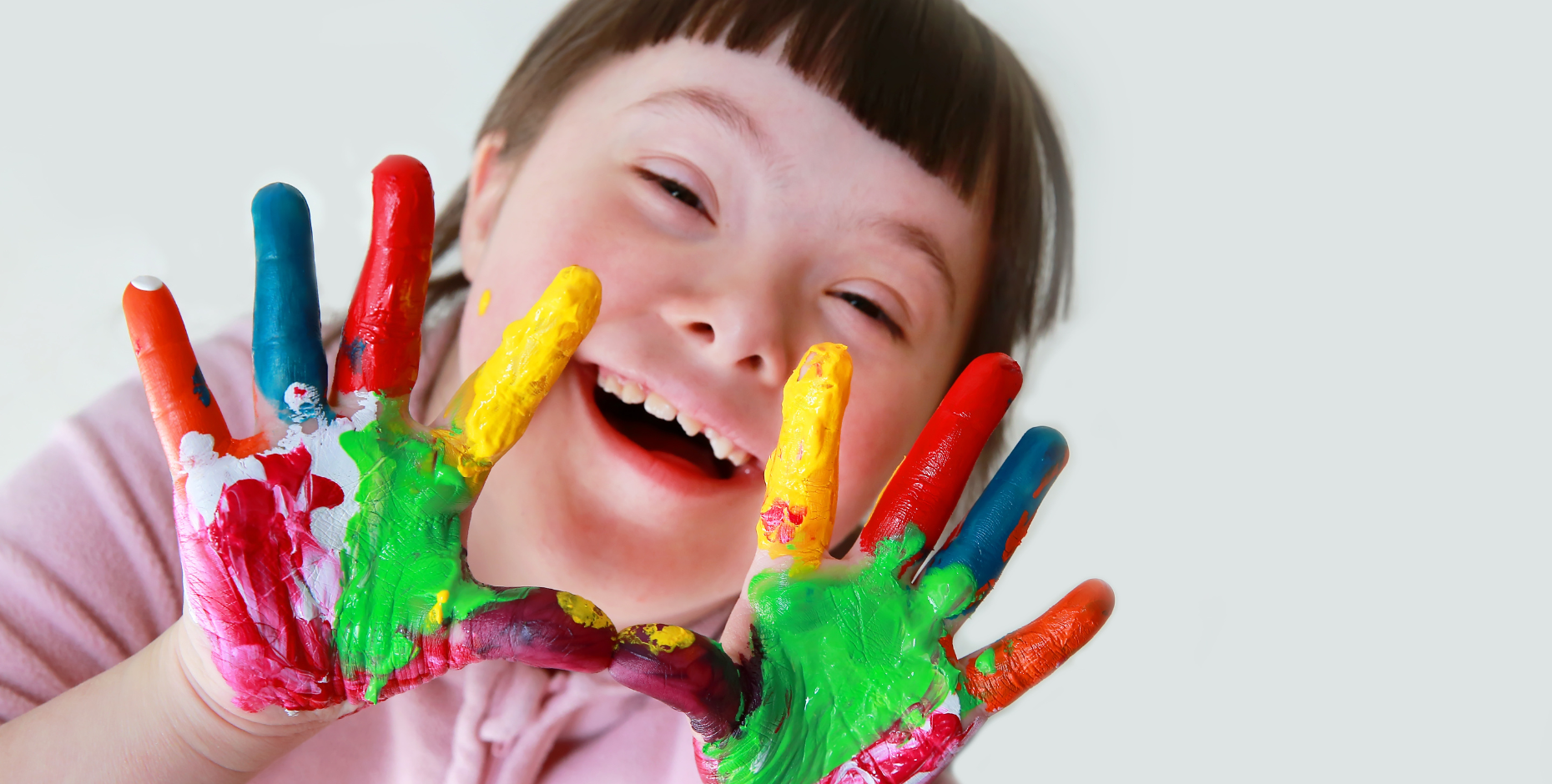 Image of a child with a disability smiling and showing paint on their hands