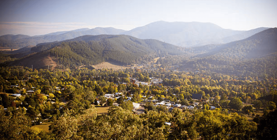 A landscape image taken from high up, not aerial but potentially from a mountain top, of a wooded valley with houses and mountains in the distance.