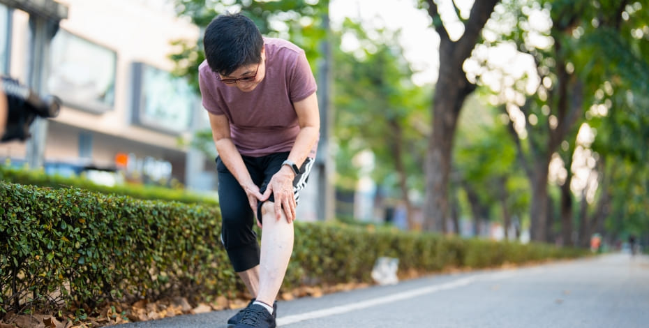 Woman clutching her knee while outside on a run. 