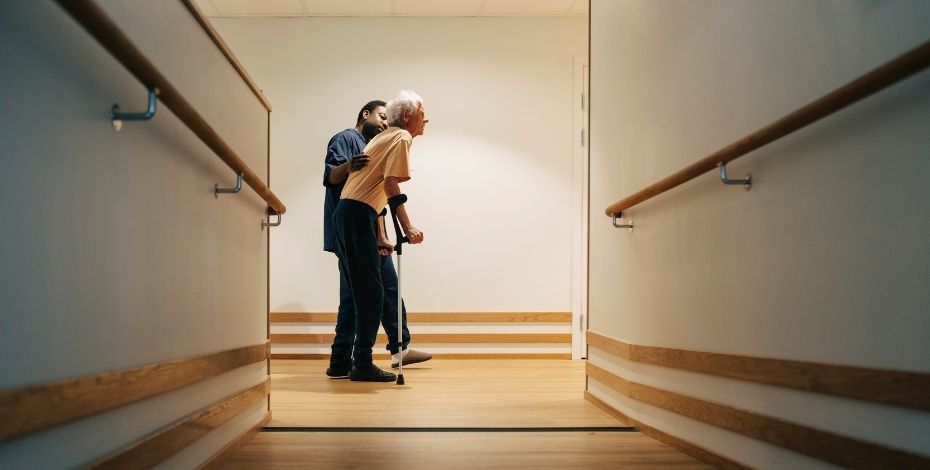 A healthcare worker helping a person to walk along a corridor
