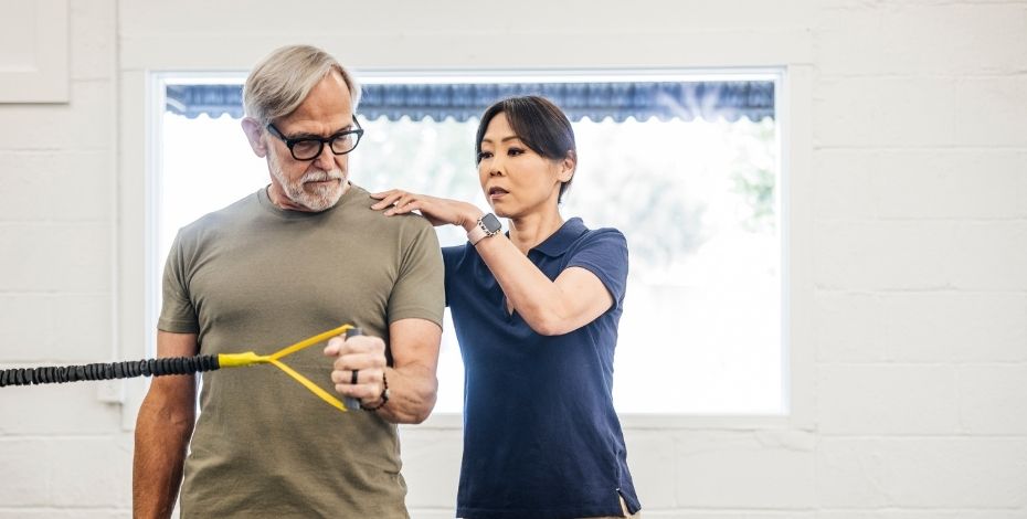 The image is of a physiotherapist standing behind a patient with hnds on their back. 