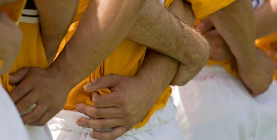 Rugby players link arms behind their backs in preparation for playing a game on the sports field. 