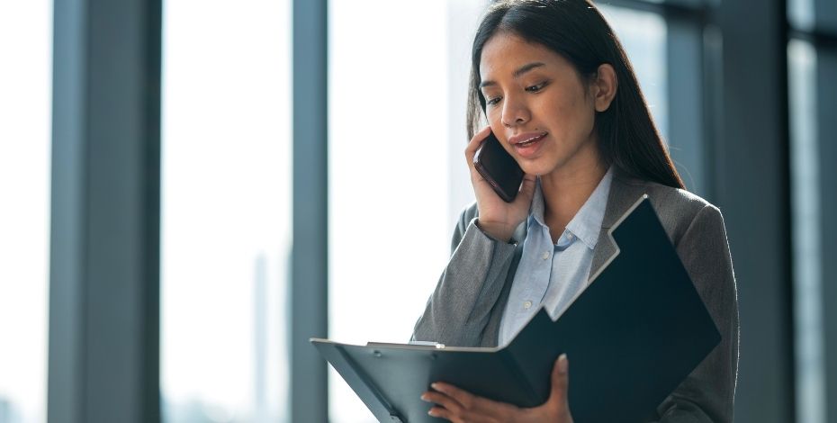 A business woman looks as though she is on the phone conducting a reference check on a potential future employee.