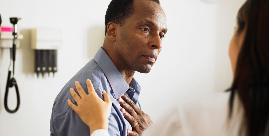 Man clutching his chest and being comforted by a health professional