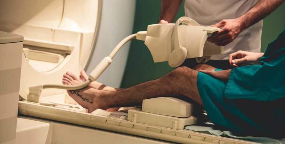 The image shows a patient about to undergo an imaging scan on his leg. A technician is holding a cover. 