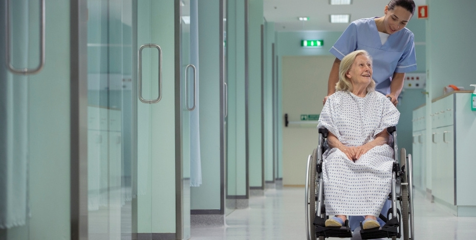 A physio pushes an elderly woman in a wheelchair
