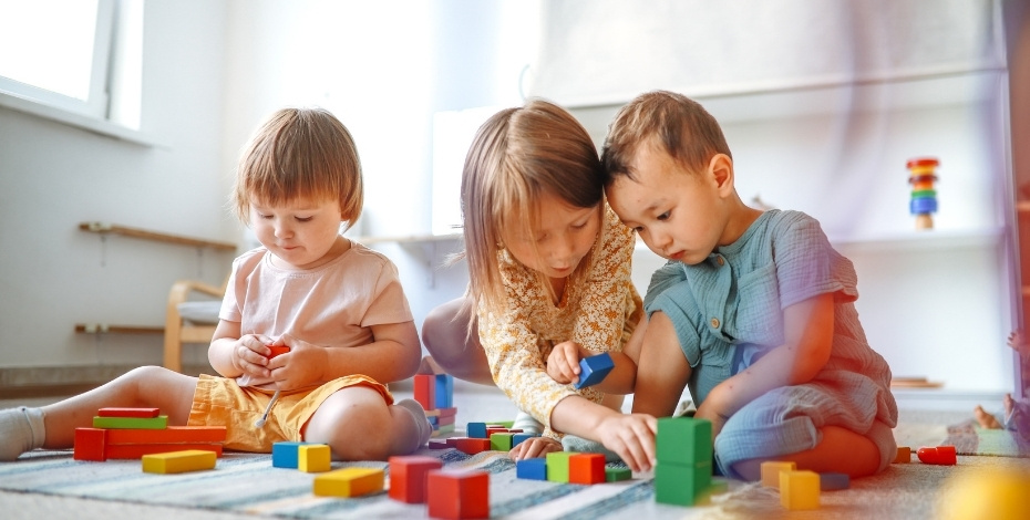 Three young children are sitting on the floor playing with building blocks. 