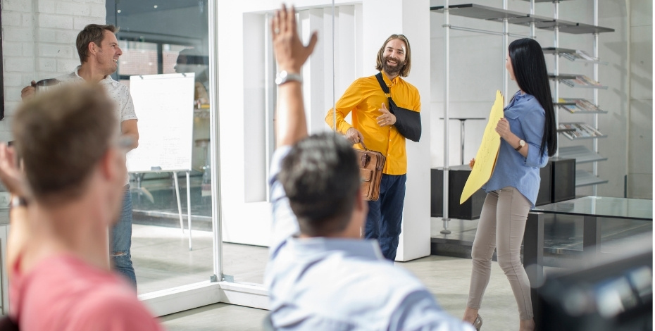 A photo of a man returning to the workplace after being injured with a broken arm. His colleagues are greeting him. 