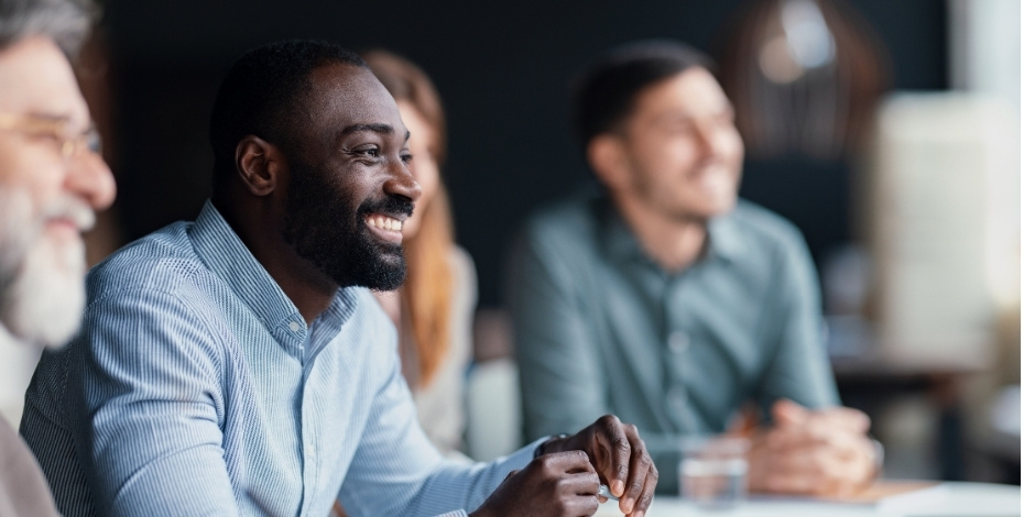 A man smiling at a table with colleagues 