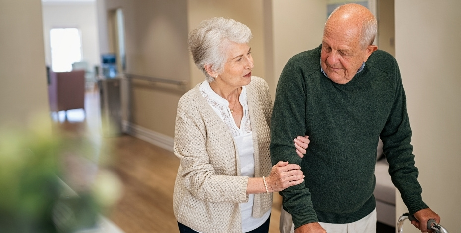 An elderly couple walking down a hospital hallway.