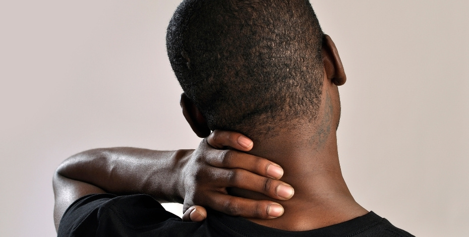 A man, seen from behind, is holding his neck. 