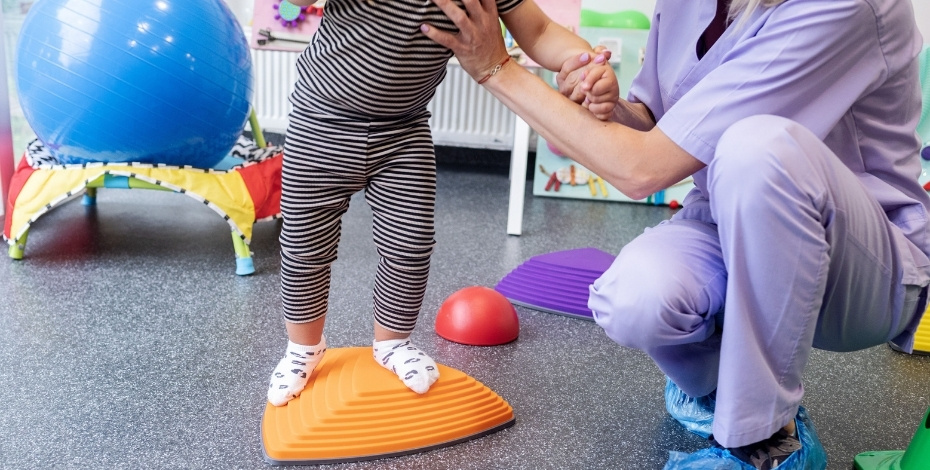 A picture of a physiotherapist helping a young child to balance.