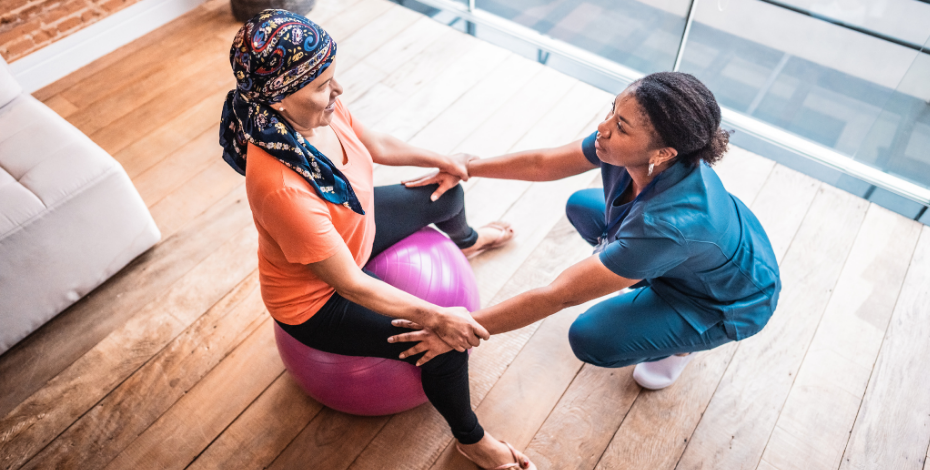 The image is of a physiotherapist holding the hands of a cancer patient sitting on an exercise ball. 