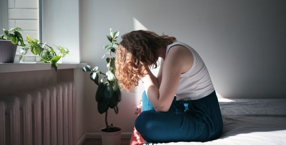 A person sitting on the edge of the bed, head in hands
