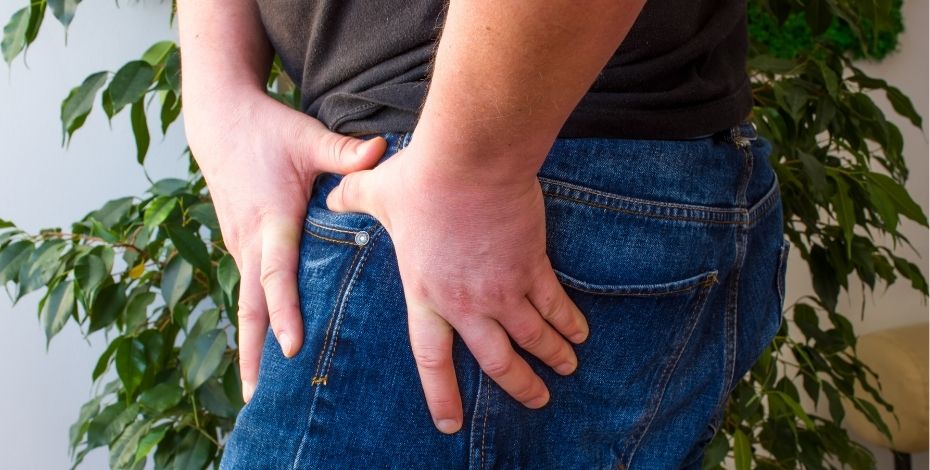 A man in jeans is holding the front of his hip/thigh. 