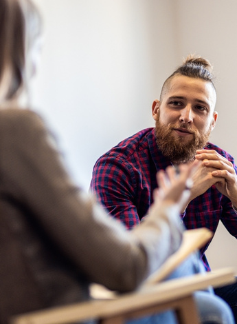 A man and woman are in conversation. The woman has a clipboard on her lap. 