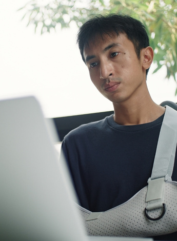 A man with a broken arm is looking at a laptop computer