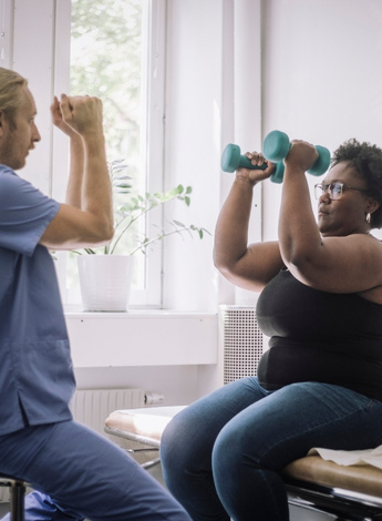 A physiotherapist is showing his patient how to do an arm exercise involving dumbbells. 