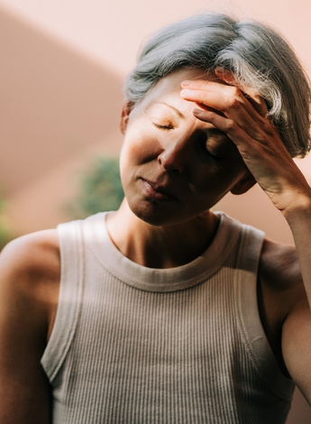 A woman tilts her head to the side and holds her hand to her forehead.