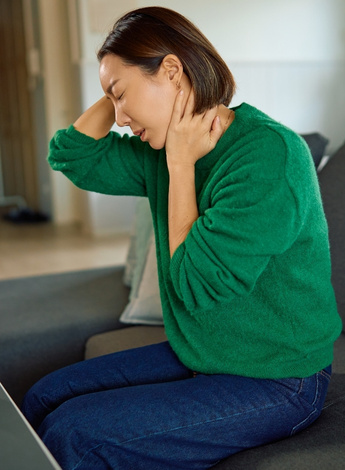A seated woman holds her neck and her head