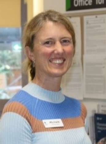 A blonde woman wearing a striped white, blue and tan top is smiling at the camera. 