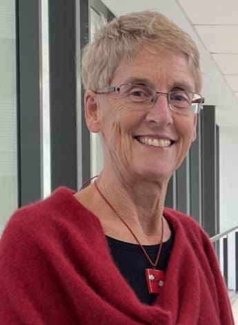 A woman with short grey hair and glasses in a red top