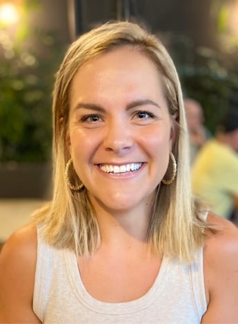 the image is of a woman with shoulder length straight blonde hair, wearing a white sleeveless top. 