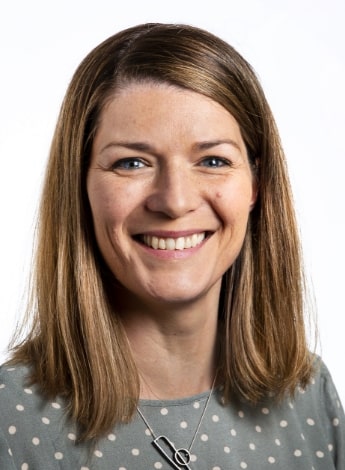 A woman with long brown hair wearing a sage green top with white polka dots