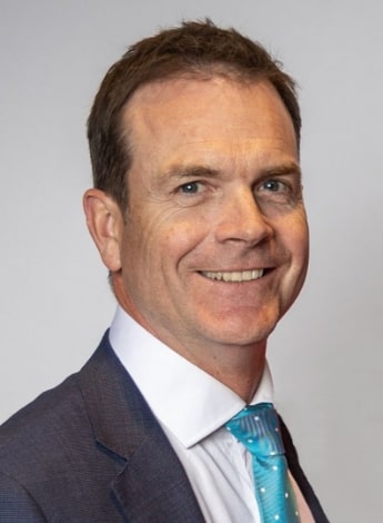 A man with dark brown hair wearing a suit with a blue tie