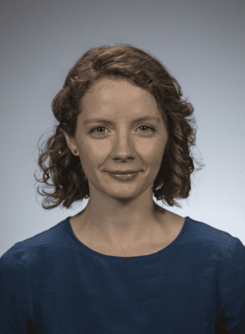 The image is a photo of Brodwen McBain. She has brown curly shoulder-length hair. 