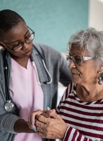 A female medical professional holds the hand of an older female patient. 