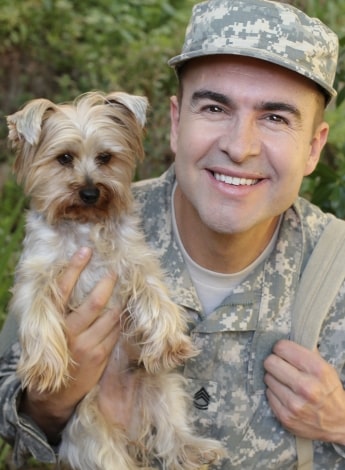 An army veteran cuddles a small dog.
