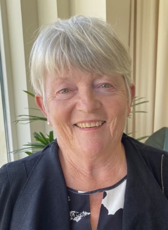 "A woman with short gray hair is looking straight at the camera. She is wearing a black and white top."