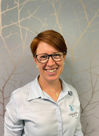 A woman with short red hair is wearing glasses and looking at the camera. 