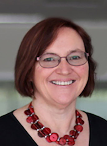 A woman with short brown hair and glasses is wearing a red necklace.