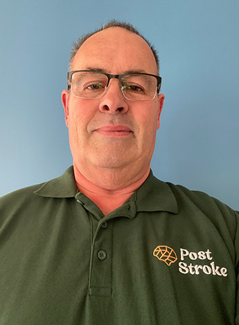 A man with short hair and glasses is wearing a green shirt and looking at the camera. 