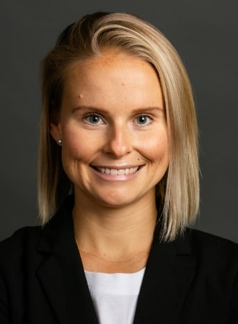 This image is of a woman with shoulder length blonde hair wearing a white shirt under a dark blazer. 