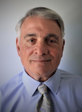 A grey haired man is wearing a blue shirt and a silver tie