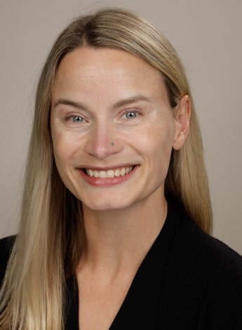 ""A woman with long blonde hair is smiling at the camera. She is wearing a black top.""