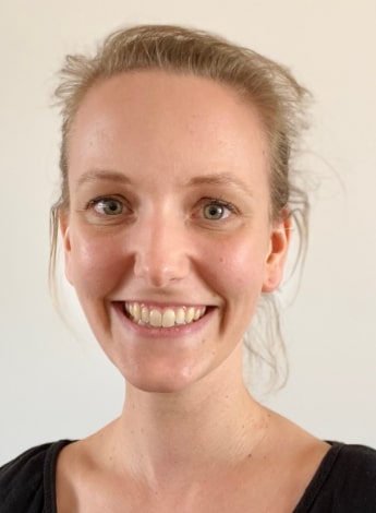 A woman with blonde hair pulled back is smiling at the camera