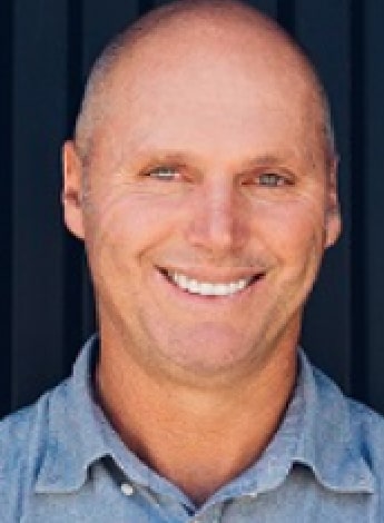 A balding man in a blue shirt smiles at the camera