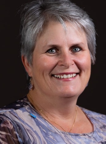 ""A woman with short gray hair  is smiling at the camera. She is wearing a purple shirt."