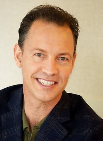 A middle-aged man wearing a blue blazer is smiling at the camera